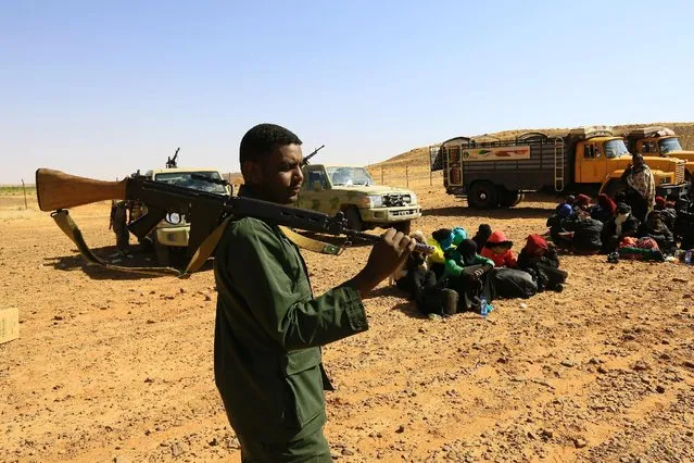 A member of Sudan's Rapid Support Forces (RSF) stands guard near illegal immigrants and traffickers, who, according to the RSF, were caught while travelling in a remote desert area en route to Libya, at Omdurman, Sudan January 8, 2017. (Photo by Mohamed Nureldin Abdallah/Reuters)