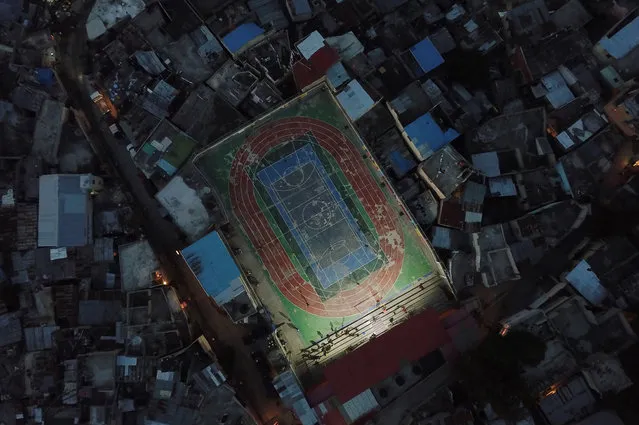 Aerial view at nightfall shows the high density of houses around a stadium in the neighborhood of Jalousie, in the commune of Petion Ville, Port-au-Prince, on December 16, 2018. Jalousie is a poor neighborhood which lacks sanitation and potable water. On the hills of Port-au-Prince, a chaotic jumble of structures stretches ever farther into the distance: Haiti's capital is suffering under the weight of high inflation, endemic corruption and a perilous drop in the value of its currency. (Photo by Héctor Retamal/AFP Photo)