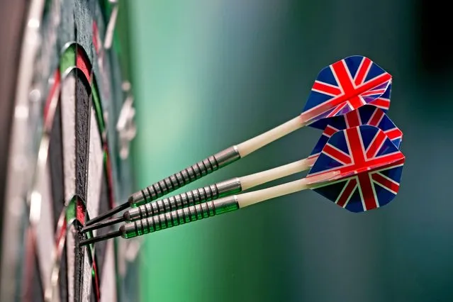 Three darts, with British union flag feathers, stick into the dart board as play continues in the quarterfinals of the World Darts Championship at Alexandra Palace in London, Monday, January 1, 2024. (Photo by Kin Cheung/AP Photo)