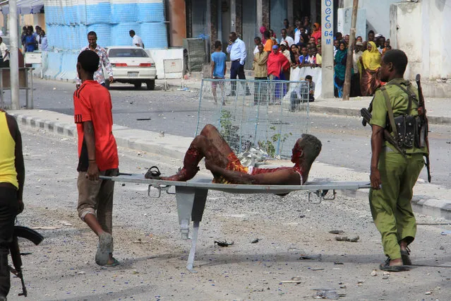 A Somali man and a soldier help a civilian who was wounded in a suicide car bomb attack on a hotel in Mogadishu, Somalia, Wednesday, January 25, 2017. (Photo by Farah Abdi Warsameh/AP Photo)