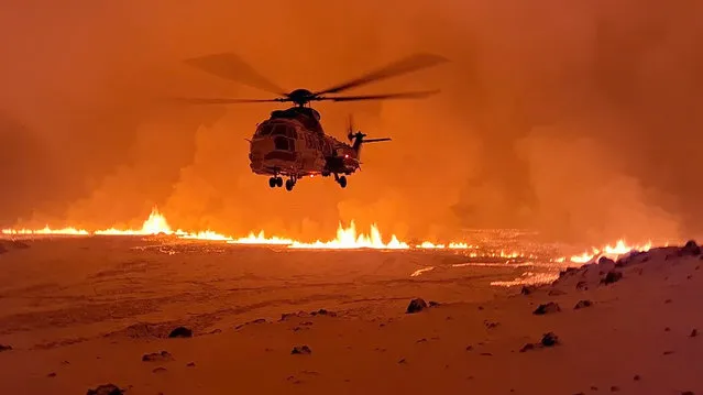 This handout image shows an Icelandic Coast Guard helicopter overflying an volcanic eruption on the Reykjanes peninsula 3 km north of Grindavik, western Iceland on December 19, 2023. A volcanic eruption began on Monday night in Iceland, south of the capital Reykjavik, following an earthquake swarm, Iceland's Meteorological Office reported. (Photo by Icelandic Coast Guard/AFP Photo)