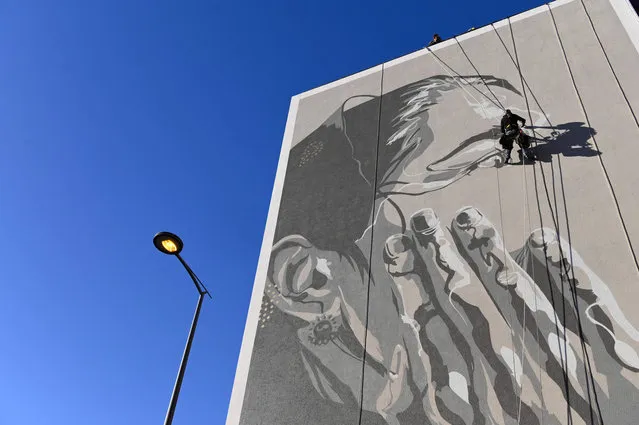 French street artist Mahn Kloix paints a mural depicting Tursunay Ziawudum, a former Uighur detainee who has left China and spoken publicly about her experience in internment, in Marseille, southern France, on October 7, 2021. The mural by Kloix has been painted on a wall of the headquarters for south-eastern France of National telecom operator Orange. (Photo by Nicolas Tucat/AFP Photo)