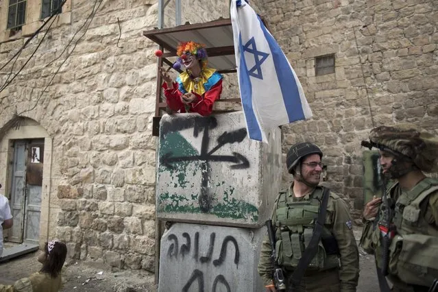 Israeli soldiers on guard as Jewish settlers in costumes march during the annual Purim parade in the Jewish part of the West Bank city of Hebron, 24 March 2016. The joyful Jewish holiday of Purim celebrates the Jews' salvation from genocide in ancient Persia, as recounted in the Scroll of Esther. The Israeli army have increased the security level, after two Palestinians were shot dead by an Israeli soldier during a stabbing incident. (Photo by Abir Sultan/EPA)