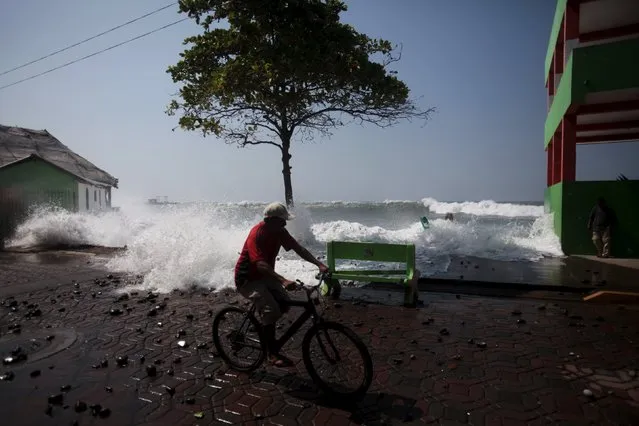 A man rides his bicycle as a wave crashes at La Libertad malecon on May 13, 2015. (Photo by Jose Cabezas/Reuters)