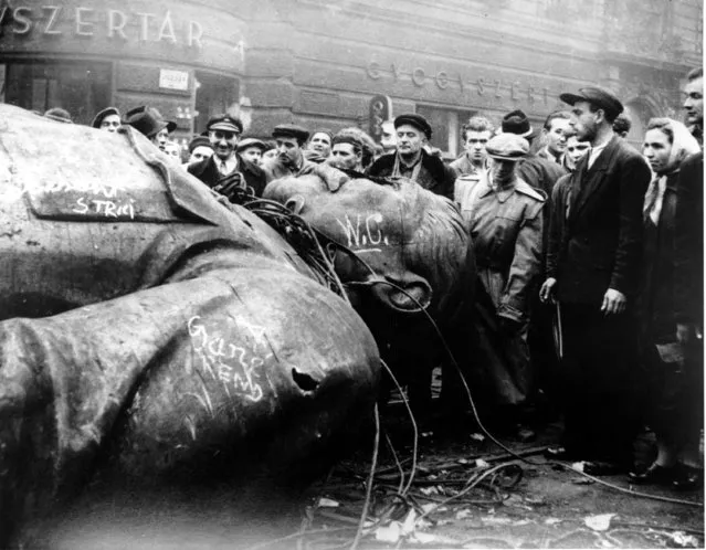 Hungarians witness the fallen statue of communist leader Josef Stalin in front of the National Theater in Budapest on October 24, 1956.  Demonstrators revolting against communist rule in Hungary pulled the statue to the ground at Dozsa Gyorgy on Oct. 23 and hauled it by tractor to Blaha Lujza where it was later smashed to pieces by the people. (Photo by Arpad Hazafi/AP Photo)