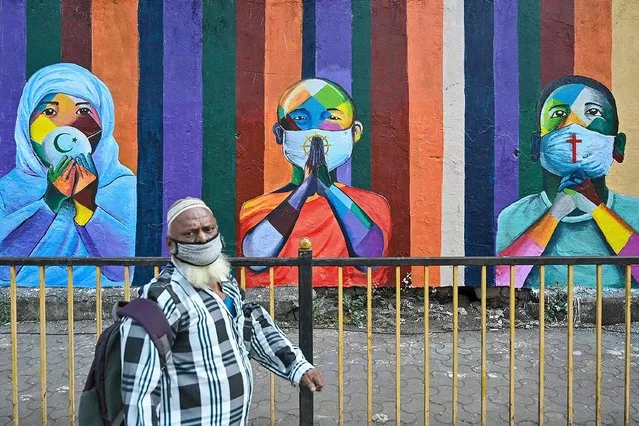 A man walks past a wall mural depiciting (L-R) a Muslim woman, a Buddhist monk and a Christian man all wearing masks to spread awareness about the Covid-19 coronavirus in Mumbai on November 17, 2021. (Photo by Punit Paranjpe/AFP Photo)