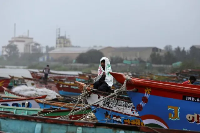 A boy covers himself from rain as he sits on a fishing boat along the shore ahead of Cyclone Vayu in Veraval, June 13, 2019. (Photo by Amit Dave/Reuters)