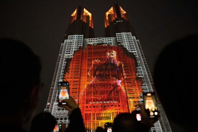People take photographs of the Tokyo Metropolitan Government building, lit up with a projection mapping titled “Godzilla: Attack on Tokyo” that shows a 100-meter tall life-size scale display of Godzilla, in Tokyo on April 27, 2024. (Photo by Yuichi Yamazaki/AFP Photo)