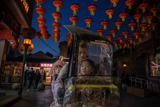 A man and two little girls ride a scooter past lanterns and decorations in the historical center of Beijing on January 27, 2022 in Beijing, China. The upcoming Beijing 2022 Winter Olympics have caused a rapid growth of the popularity of winter sports and winter outdoor activities in China. (Photo by Andrea Verdelli/Getty Images)