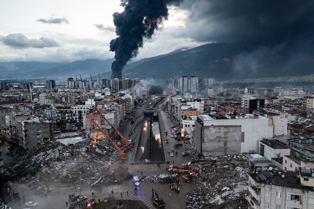 Smoke billows from the Iskenderun Port as rescue workers work at the scene of a collapsed building on February 07, 2023 in Iskenderun, Turkey. A 7.8-magnitude earthquake hit near Gaziantep, Turkey, in the early hours of Monday, followed by another 7.5-magnitude tremor just after midday. The quakes caused widespread destruction in southern Turkey and northern Syria and were felt in nearby countries. (Photo by Burak Kara/Getty Images)