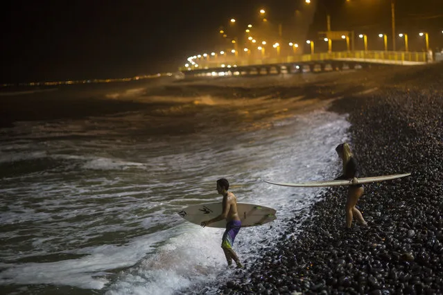 In this March 1, 2017 photo, surfers walk over the rocky shore into the Pacific Ocean at La Pampilla beach in Lima, Peru. The beach attracts fewer than two dozen surfers a night. (Photo by Rodrigo Abd/AP Photo)