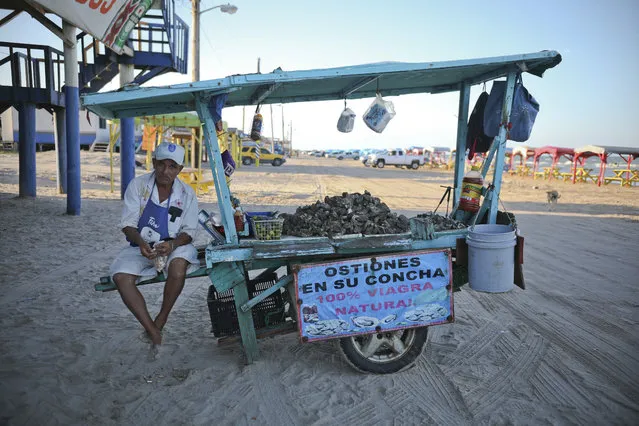In this August 2, 2019 photo, an oyster vendor snacks on shelled peanuts while he waits for customers in Playa Bagdad near the border city of Matamoros, Mexico. Here, the landscape is not one of walls or border guards; it is simply miles of dunes and Gulf coast beaches, marked only by simple wooden huts or awnings held up by sticks. (Photo by Emilio Espejel/AP Photo)