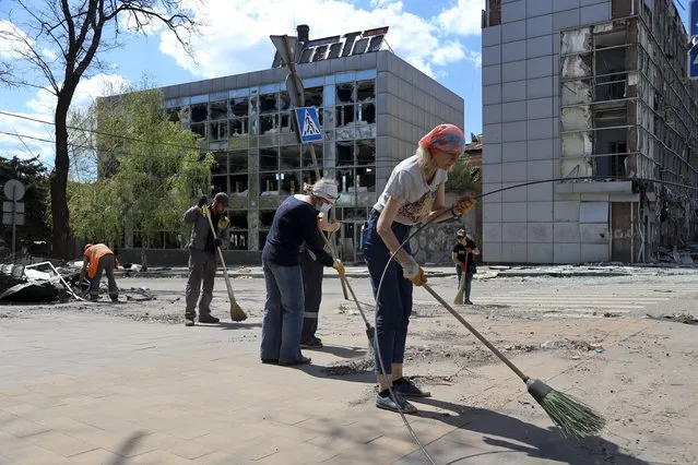 Volunteers clean a street next to damaged buildings in Mariupol, in territory under the government of the Donetsk People's Republic, eastern Ukraine, Wednesday, April 27, 2022. Municipal services and volunteers began clearing rubble and cleaning the city. (Photo by Alexei Alexandrov/AP Photo)