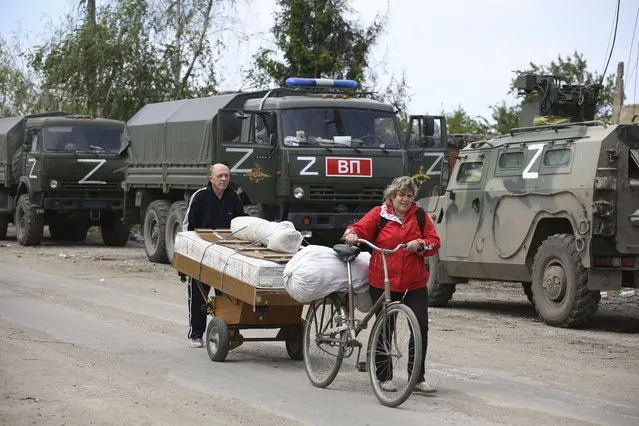 Local residents walk past Russian military vehicles in Mariupol, in territory under the government of the Donetsk People's Republic, eastern Ukraine, Tuesday, May 17, 2022. (Photo by Alexei Alexandrov/AP Photo)