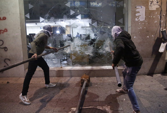 Anti-government protesters smash a bank widow, during ongoing protests against the Lebanese central bank's governor and against the deepening financial crisis, at Hamra trade street, in Beirut, Lebanon, Tuesday, January 14, 2020. Lebanese security forces lobbed tear gas at protesters who responded with rocks outside the country's central bank Tuesday, a violent turn after demonstrators returned to the streets following a weekslong lull. (Photo by Hussein Malla/AP Photo)
