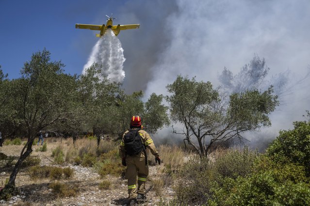 An aircraft drops water over a wildfire in Vati village, on the Aegean Sea island of Rhodes, southeastern Greece, on Tuesday, July 25, 2023. A third successive heat wave in Greece pushed temperatures back above 40 degrees Celsius (104 degrees Fahrenheit) across parts of the country Tuesday following more nighttime evacuations from fires that have raged out of control for days. (Photo by Petros Giannakouris/AP Photo)