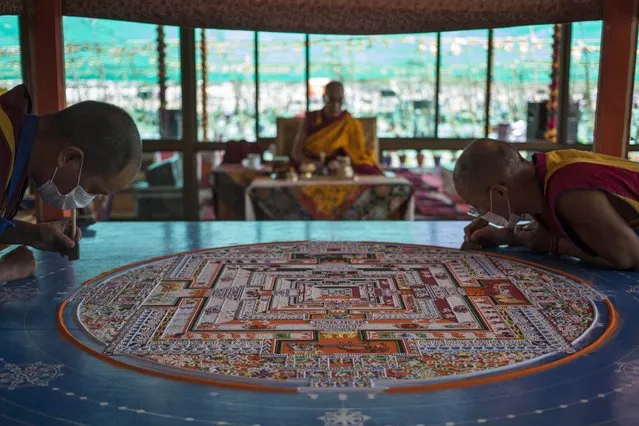 Buddhist monks prepare a Sand Mandala, a spiritual and ritual symbol depicting the Buddhist universe, as Tibetan spiritual leader the Dalai Lama is seated at the back on the fifth day of Kalachakra near Leh, India, Monday, July 7, 2014. Buddhist devotees from across the globe have arrived in this Himalayan region of Ladakh to attend the “Kalachakra” or Wheel of Time initiations by the Dalai Lama that began Thursday. (Photo by Tsering Topgyal/AP Photo)