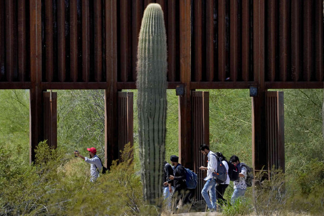 A group claiming to be from India walk past open border wall storm gates after crossing through the border fence in the Tucson Sector of the U.S.-Mexico border, Tuesday, August 29, 2023, in Organ Pipe Cactus National Monument near Lukeville, Ariz. Migrants walk through storm gates currently open in the towering wall of steel bollards due to possible rains during the monsoon season that ends in two weeks. There were several heavy downpours in the area this year and CBP said rushing water can damage the gates, wall, border road, and local flora and fauna. (Photo by Matt York/AP Photo)