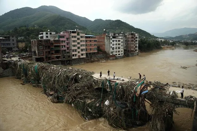 This photo taken on July 10, 2016 shows residents walking over a bridge covered in debris in the aftermath of a tropical storm in Bandong town, in Minqing county, east China's Fujian province. (Photo by AFP Photo/Stringer)