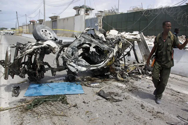 Somali soldier stand near the wreckage of a car bomb outside the UN's office in Mogadishu, Somalia, Tuesday, July 26, 2016. A suicide bomber detonated an explosives-laden car outside the United Nations Mine Action Service offices in Mogadishu, killing 13 people, including seven U.N. guards, a Somali police official said. (Photo by Farah Abdi Warsameh/AP Photo)