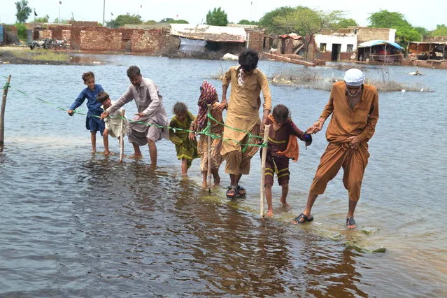 People wade through a flooded area following heavy rains in Sanghar District, Sindh province, Pakistan, 28 August 2022. According to the National Disaster Management Authority (NDMA) on 27 August, flash floods triggered by heavy monsoon rains have killed over 1,000 people across Pakistan since mid-June 2022. More than 33 million people have been affected by floods, the country's climate change minister said. (Photo by Nadeem Khawar/EPA/EFE)