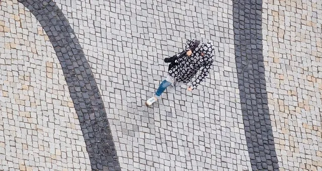 A woman in a raincoat walks during rainy weather over the Trammplatz place in Hannover, northern Germany, Tuesday, August 2, 2016. (Photo by Julian Stratenschulte/DPA via AP Photo)