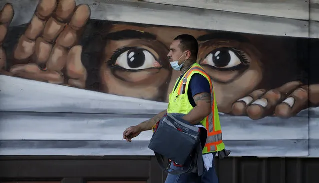 A construction worker walks past a mural painted on a boarded up business that is temporarily closed due to the COVID-19 pandemic Monday, April 27, 2020, in Austin, Texas. Texas Gov. Greg Abbott announced he is relaxing some restrictions that have been imposed on some businesses. (Photo by Eric Gay/AP Photo)