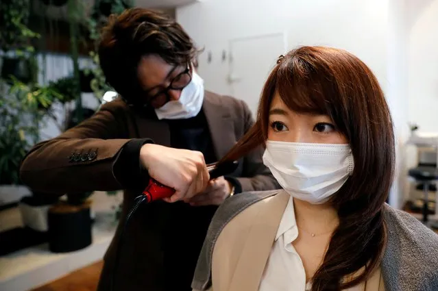 Akihiro Yoshida, the owner of Hair salon Pinch, gives hair treatment to his customer Natsuki Suda, while both of them wear protective face masks in order to prevent infections following the coronavirus disease (COVID-19) outbreak, in Tokyo, Japan, April 28, 2020. According to Yoshida, the revenue of his salon in April falls less than 50 percent of usual season and now it accepts one customer at a time by appointment only as a measurement for preventing the infection. (Photo by Kim Kyung-Hoon/Reuters)