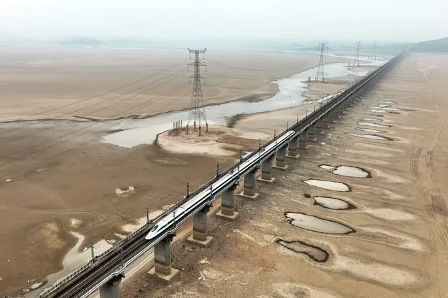 This aerial photo taken on September 22, 2022 shows a train driving on a bridge above a dry area of China's largest freshwater Poyang Lake in Jiujiang, in China's central Jiangxi province. (Photo by AFP Photo/China Stringer Network)