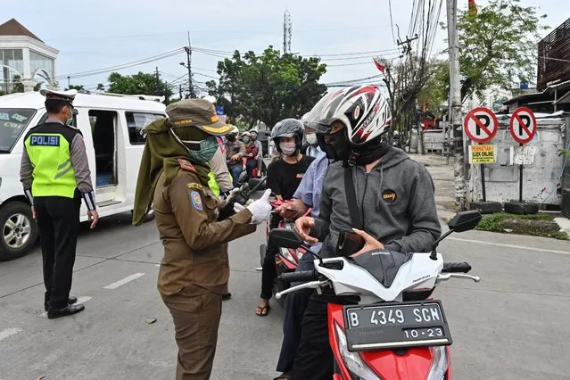 An officer of Jakarta's city order agency checks documents of motorists at a check point during a partial lockdown to curb the spread of the COVID-19 coronavirus in Jakarta on May 11, 2020. (Photo by Adek Berry/AFP Photo)