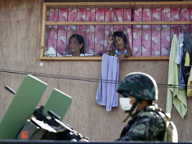 Filipino residents inside a shanty view a police officer wearing a facemask on top of an armored personnel carrier during a lockdown in Navotas City, Philippines, 16 July 2020. According to reports, Navotas City will go back into a two week lockdown starting on 16 July, to contain the surge of coronavirus infections. (Photo by Francis R. Malasig/EPA/EFE)