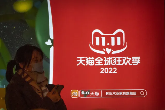 A woman waits for a bus at a bus stop next to an advertisement for Tmall's Singles' Day sale in Beijing, Wednesday, November 9, 2022. China's biggest online shopping festival, known as Singles' Day, is typically an extravagant affair as Chinese e-commerce firms like Alibaba and JD.com ramp up marketing campaigns and engage top livestreamers to hawk everything from lipstick to furniture as they race to break sales records of previous years. (Photo by Mark Schiefelbein/AP Photo)