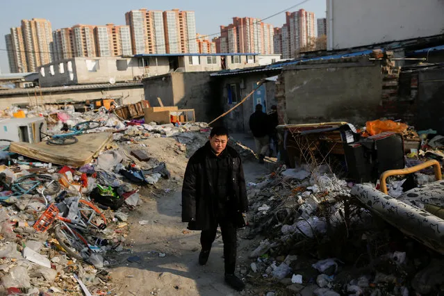 A man walks between the debris of demolished houses the Baiqiangzi migrant village as apartment highrises are seen in the background in Beijing, China, December 13, 2017. (Photo by Thomas Peter/Reuters)