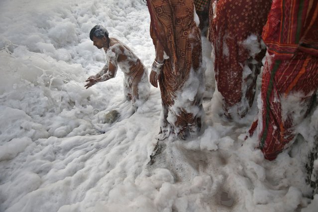 A Hindu devotee pushes the foam away to make space for other devotees to worship the Sun god Surya in the polluted waters of the river Yamuna during the Hindu religious festival of Chatt Puja in New Delhi October 30, 2014. Hindu women fast for the whole day for the betterment of their family and the society during the festival. (Photo by Ahmad Masood/Reuters)