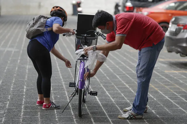 A recipient, left, of a bicycle from the Benjamin Canlas Courage to be Kind Foundation prepares to ride outside a building at the financial district of Manila, Philippines, Saturday, July 11, 2020. Restricted public transportation during the lockdown left many Filipinos walking for hours just to reach their jobs. The foundation saw the need and gave away mountain bikes to nominated individuals who are struggling to hold on to their jobs in a country hard hit by the coronavirus. (Photo by Aaron Favila/AP Photo)