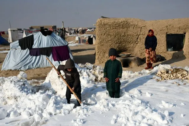 Afghan internally-displaced children shovel snow near their tents during a cold winter day at Nahr-e Shah-e- district of Balkh Province, near Mazar-i-Sharif on January 17, 2023. At least 70 people have died in a wave of freezing temperatures sweeping Afghanistan, officials said on Janaury 18, as extreme weather compounds a humanitarian crisis in the poverty-stricken nation. (Photo by Atif Aryan/AFP Photo)