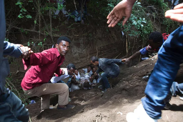 People extract an injured man from a ditch after a deadly stampede during the Oromo new year holiday Irreechaa in Bishoftu on October 2, 2016. Several people were killed in a stampede near the Ethiopian capital on October 2, according to an AFP photographer at the scene. Several thousand people from the Oromo community gathered at a sacred lake for a religious festival and started to cross their wrists above their heads, a symbol of Oromo anti-government protests. The event quickly degenerated, with protesters throwing stones and bottles and security forces responding with baton charges and tear gas grenades. Together, Oromos and Amharas make up 60 percent of the population and have become increasingly vocal in rejecting what they see as the disproportionate power wielded by the northern Tigrean minority in government and the security forces. (Photo by Zacharias Abubeker/AFP Photo)
