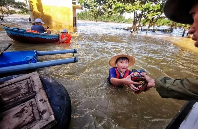 A boy gets food donation from a volunteer at a flooded area in Quang Binh province, Vietnam on October 21, 2020. (Photo by Thanh Dat/VNA via Reuters)