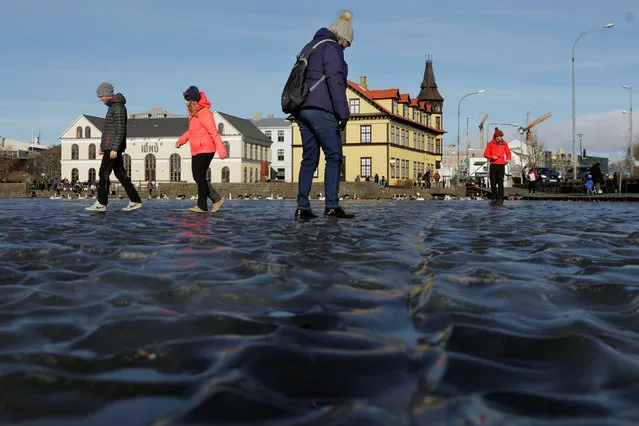 Tourists walk across water frozen into a ripple pattern on Tjornin Pond in Reykjavik, Iceland, March 11, 2018. (Photo by Lucas Jackson/Reuters)