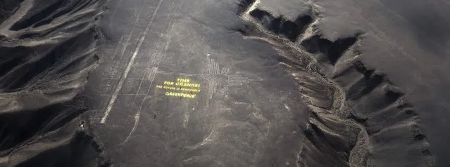 Greenpeace activists stand next  to massive letters delivering the message “Time for Change: The Future is Renewable” next to the hummingbird geoglyph in Nazca in Peru, Monday, December 8, 2014. (Photo by Rodrigo Abd/AP Photo)