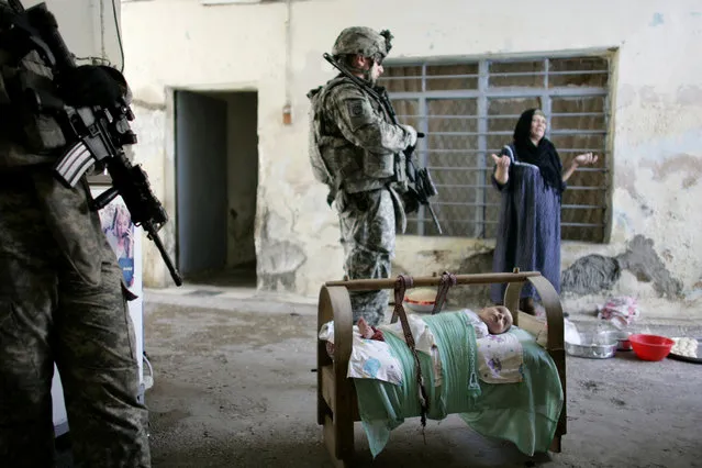 An Iraqi baby lies in a cradle while a woman argues with U.S. soldiers of 1/8 Bravo Company searching for weapons, explosives and information about militants in the area during a foot patrol in a neighbourhood of Mosul, June 26, 2008. (Photo by Eduardo Munoz/Reuters)