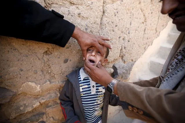 A boy is being held by relatives as he waits to receive polio vaccine drops during a house-to-house vaccination campaign in Yemen's capital Sanaa, November 10, 2015. (Photo by Khaled Abdullah/Reuters)