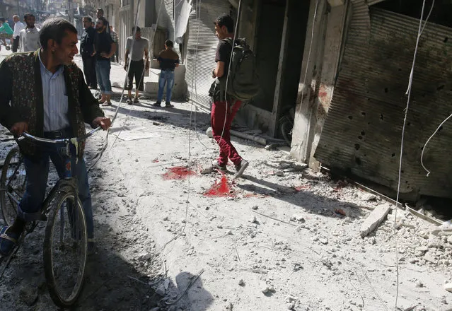People inspect the damage as a civilian walks near bloodstains at a market hit by air strikes in Aleppo's rebel-held al-Fardous district, Syria October 12, 2016. (Photo by Abdalrhman Ismail/Reuters)