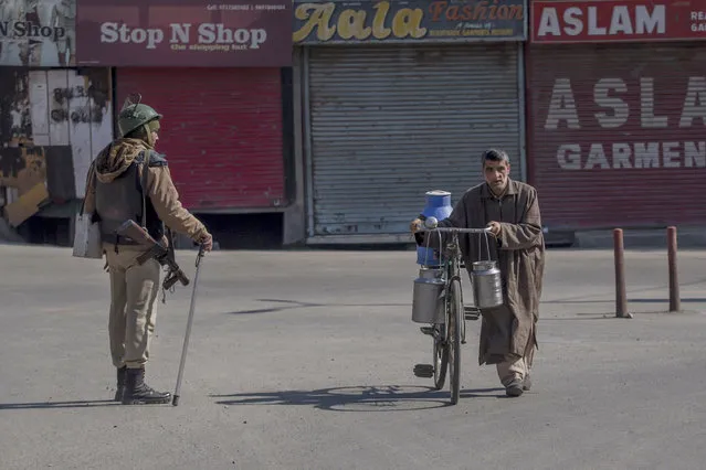 Kashmiri milk man walks his bicycle past an Indian paramilitary soldier during restrictions in Srinagar, Indian-controlled Kashmir, Wednesday, March 7, 2018. (Photo by Dar Yasin/AP Photo)