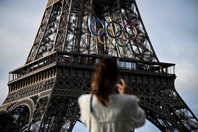 A woman takes a picture of the Eiffel Tower decorated with the Olympic rings for the upcoming Paris 2024 Olympic Games, in Paris, on June 17, 2024. (Photo by Julien de Rosa/AFP Photo)
