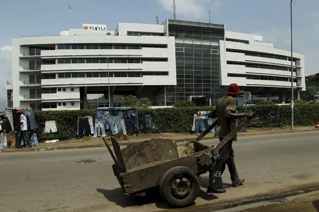 A man carries wood in a cart past the Ivory Coast headquarters of the Bollore group in Abidjan, Ivory Coast, November 12, 2015. A major West African rail scheme being built by French industrial conglomerate Bollore is caught up in a legal action, initiated by a rival firm shortly after the group hired banks to prepare for a Paris bourse listing of the regional project. (Photo by Luc Gnago/Reuters)