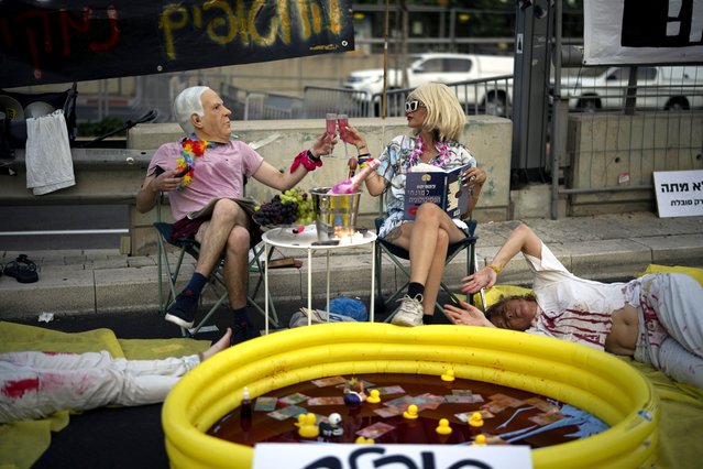 People wear costumes depicting Israeli Prime Minister Benjamin Netanyahu and his wife as demonstrators lie on the ground painted in red, symbolizing blood, during a protest against his government and call for the release of hostages held in the Gaza Strip by the Hamas militant group, in Tel Aviv, July 20, 2024. (Photo by Leo Correa/AP Photo)