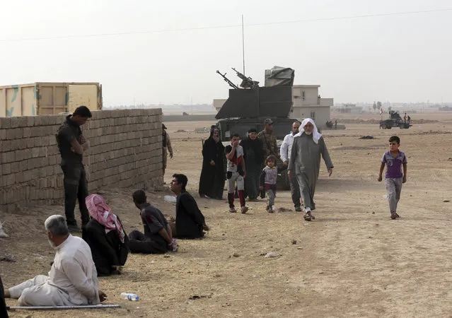 Civilians leave their houses as a member of Iraq's elite counterterrorism forces interrogates handcuffed suspects of Islamic State in the village of Tob Zawa, about 9 kilometers (5½ miles) from Mosul, Iraq, Tuesday, October 25, 2016. Around 335 civilians were evacuated to a refugee camp from the village, which was retaken by special forces on Monday, Maj. Gen. Haider Fadhil said. He said the civilians were relocated to protect them from possible IS shelling. (Photo by Khalid Mohammed/AP Photo)