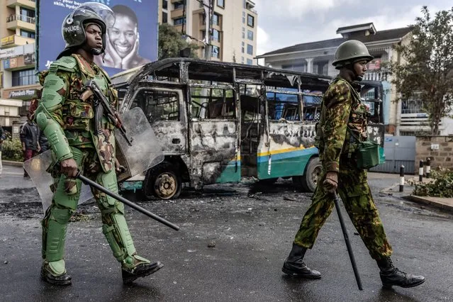 Kenyan police officer walk next to a bus burnt by protesters during riots in Nairobi on May 2, 2023. Kenyan riot police were out on the streets on May 2, 2023 as the opposition defied a police ban and staged new demonstrations over the cost of living crisis and last year's election results. (Photo by Luis Tato/AFP Photo)