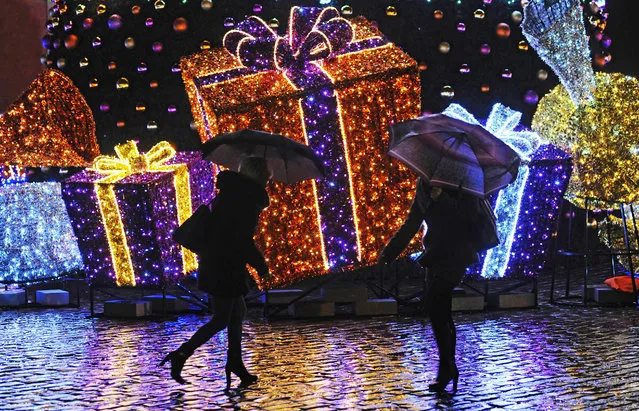 People walk past Seasonal decorations on a rainy evening in Warsaw, Poland, Tuesday, December 23, 2014, one day ahead of Christmas Eve. Weather forecasts predict a rainy Christmas in Poland. (Photo by Alik Keplicz/AP Photo)